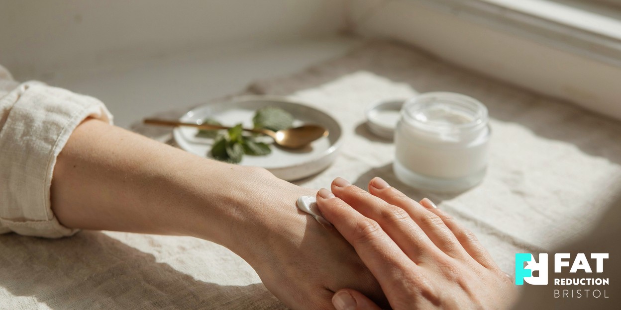 Close-up photograph of a person’s hands gently smoothing a rich moisturising cream into their forearm, soft natural daylight, warm neutral tones